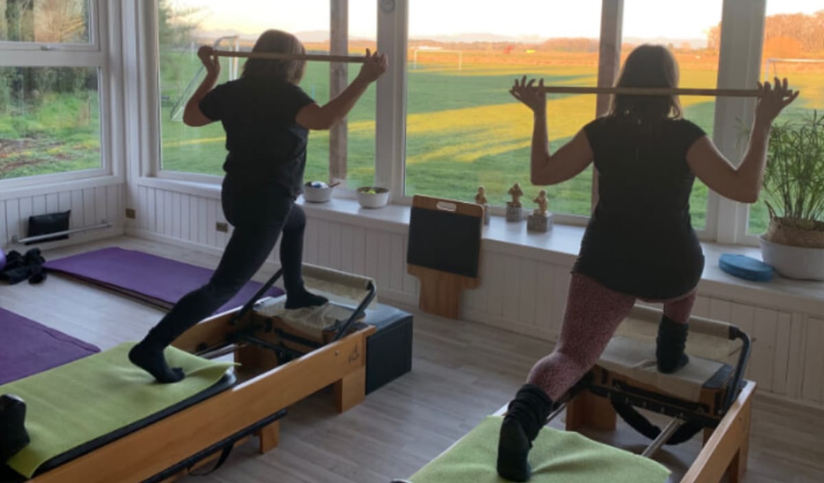Clase de pilates con máquinas junto a ventanales al jardín